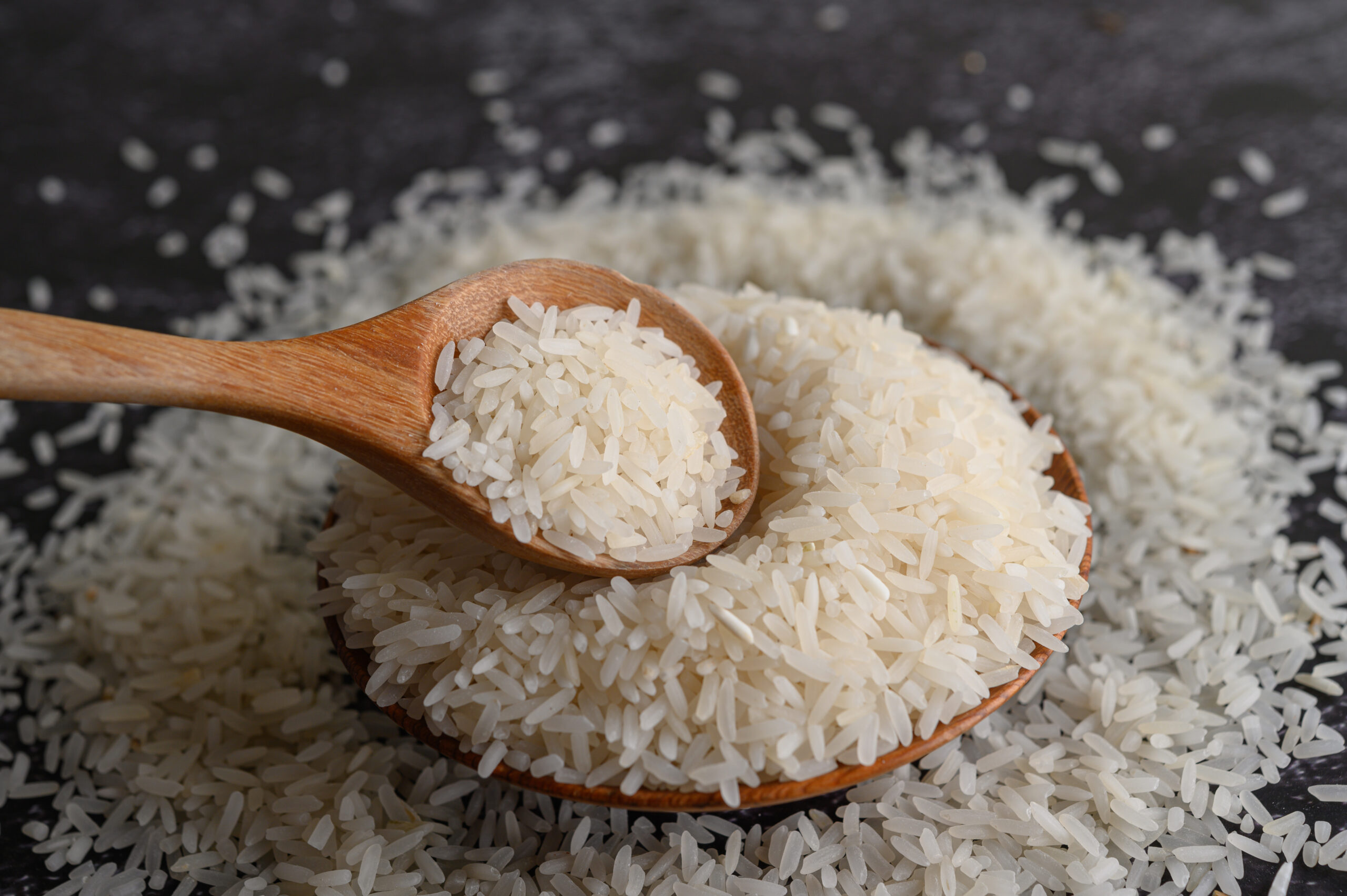 Milled rice in a bowl and a wooden spoon on the black cement flo
