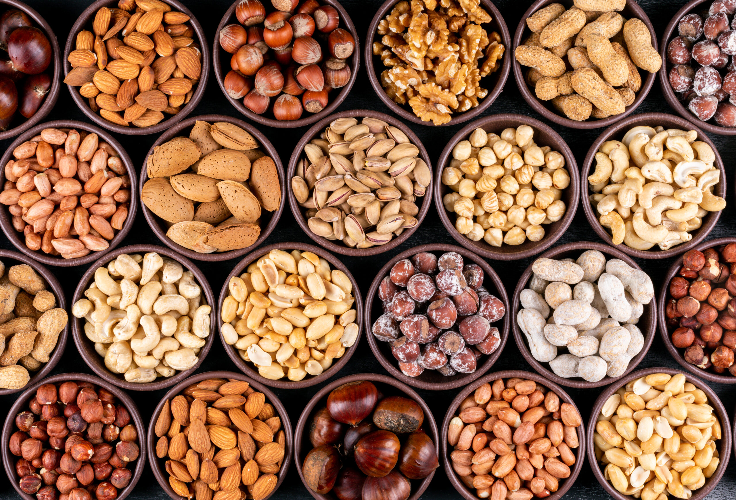Set of pecan, pistachios, almond, peanut, cashew, pine nuts and lined up assorted nuts and dried fruits in a mini different bowls on a black stone background. flat lay.