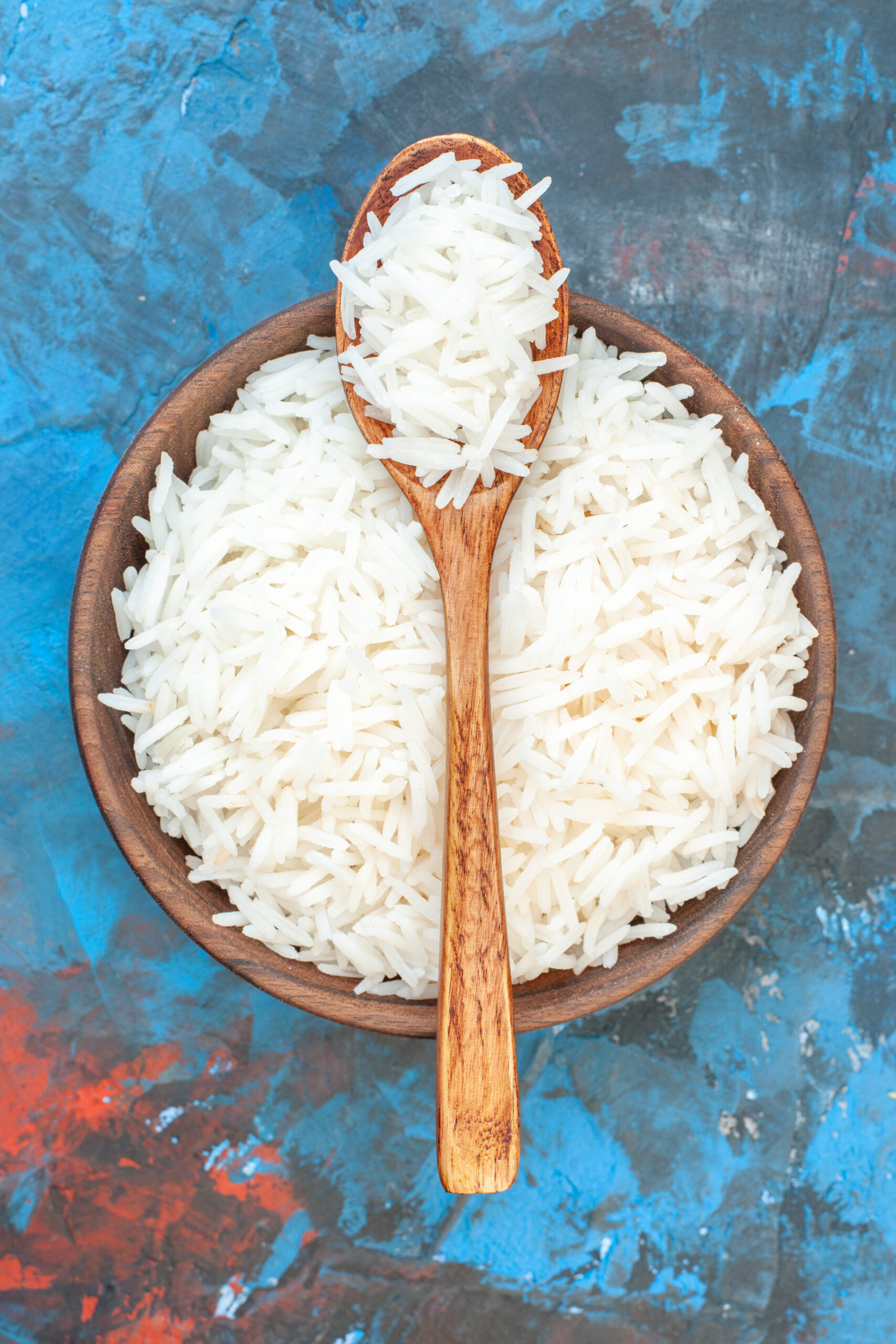 vertical-view-tasty-rice-meal-brown-small-pot-wooden-spoon-blue-background